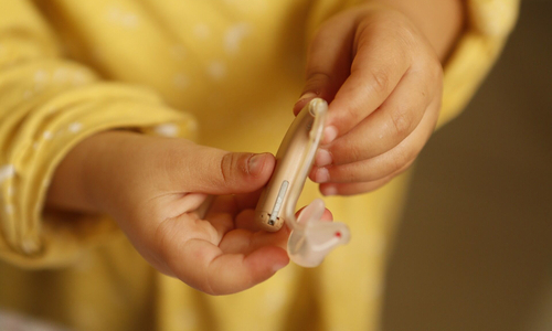 on voit les mains d'un enfant d'environ 2 ans avec un pyjama jaune porter un appareil auditif 