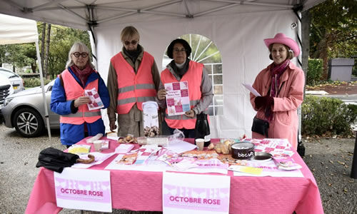 Quatre femmes portent un vêtements rose et présentent des flyers derrière un stand pour l'opération octobre rose