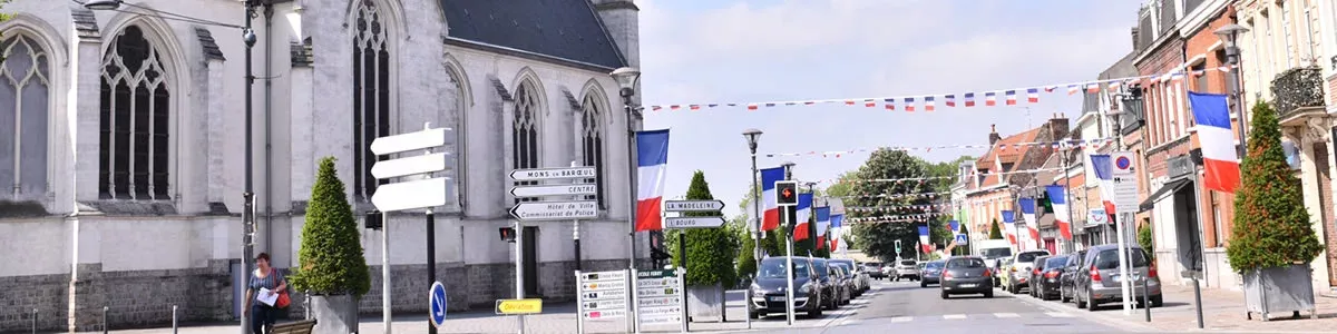 L'église Saint Vincent, une église en pierres blanches à gauche et une rue avec des drapeaux multicolores 