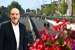 Jean Louis Munch , un homme avec une veste de costume bleu marine  se tient le devant  le grand boulevard ou des personnes se promènent. Des fleurs rouges au premier plan droit sont également présentes
