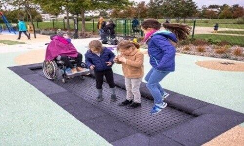3 enfants sautent sur un trampoline et un enfant en fauteuil roulant