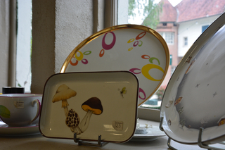 Un petit plat rectangulaire en porcelaine décoré de champignons est exposé avec deux assiettes en porcelaine en arrière plan